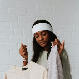 A young woman in a headband carefully selects clothes on hangers inside a bright loft space.