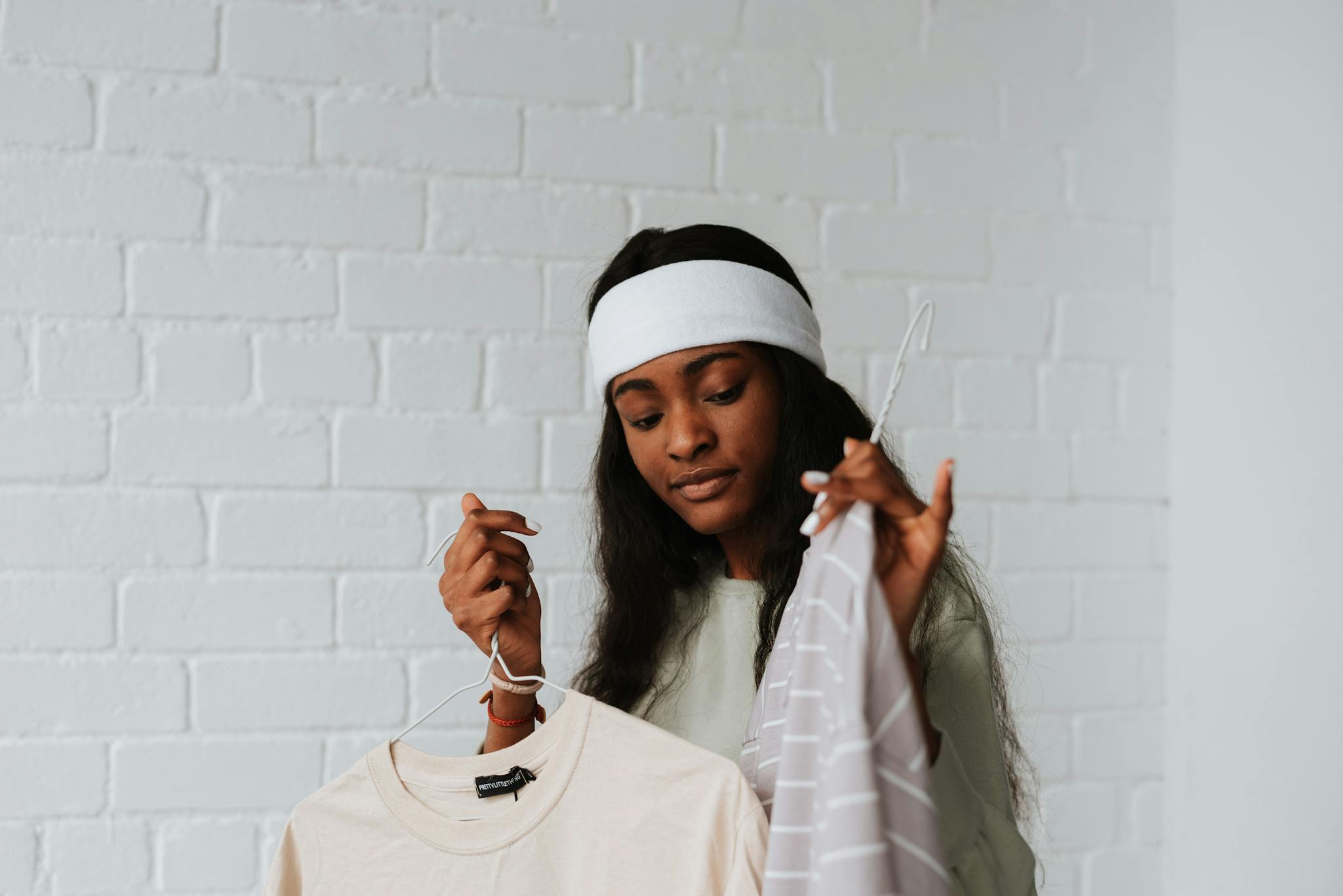 A young woman in a headband carefully selects clothes on hangers inside a bright loft space.