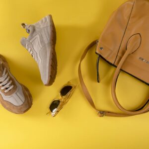 Stylish brown handbag, fashionable eyewear, and sport shoes on vibrant yellow background.