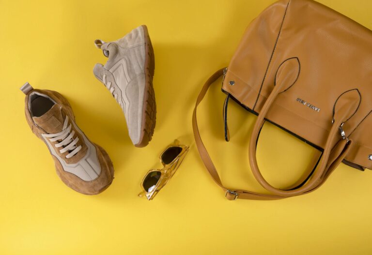 Stylish brown handbag, fashionable eyewear, and sport shoes on vibrant yellow background.
