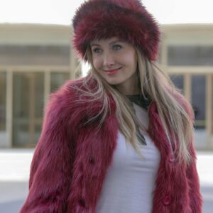 Stylish woman wearing a red fur hat and coat, casually standing in a city environment.