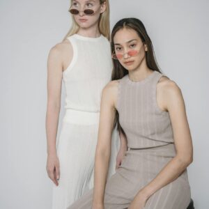 Two women in stylish outfits posing in a minimalist studio setting.