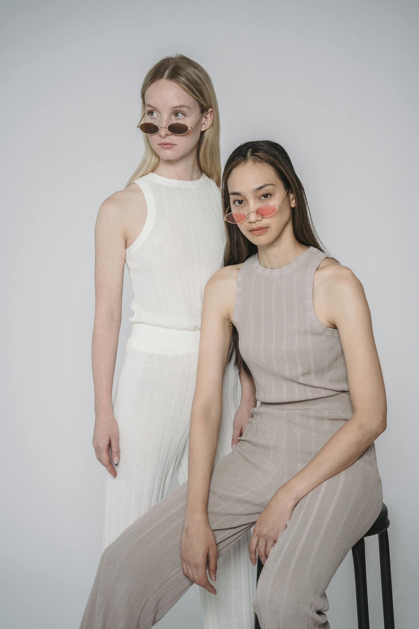 Two women in stylish outfits posing in a minimalist studio setting.